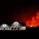 A nighttime view of a ranch house with a forest fire burning in the background