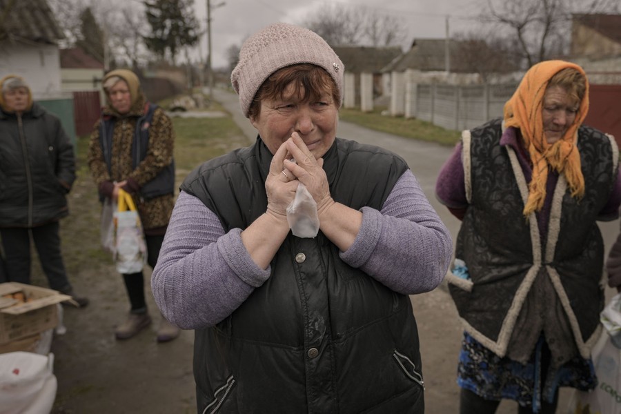 Several people stand on a street, waiting for food handouts.