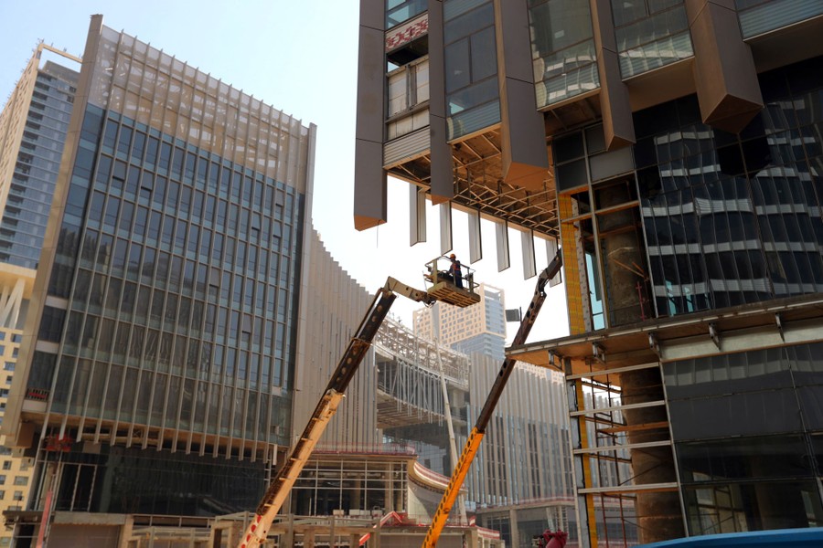 Workers stand on lifts among several large buildings under construction.