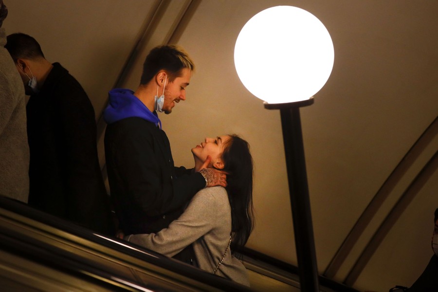A young couple embrace and look at each other while riding an escalator.