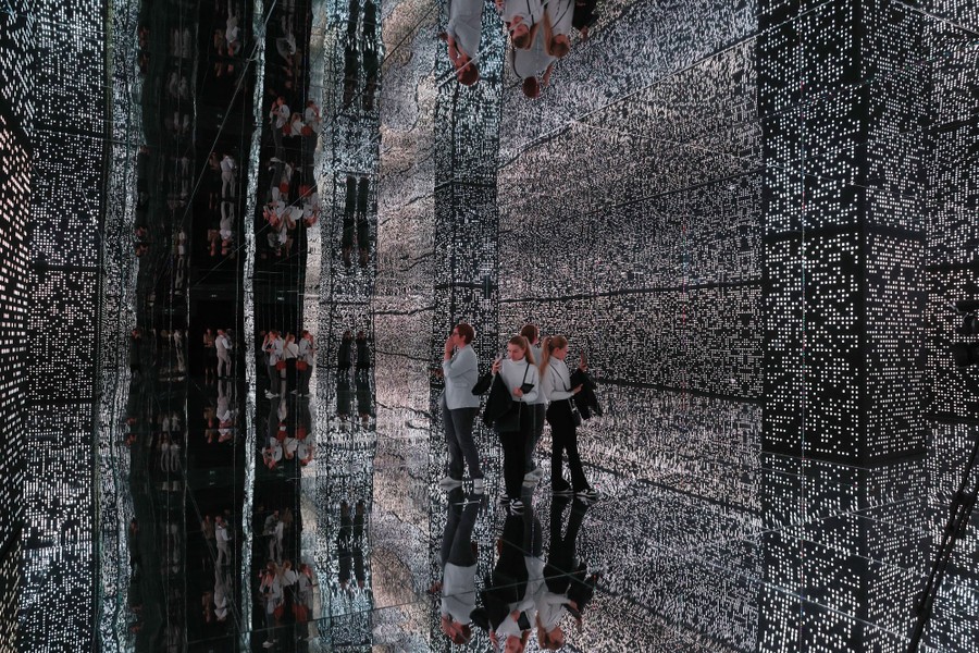 Several people stand in a room covered in lights and mirrors