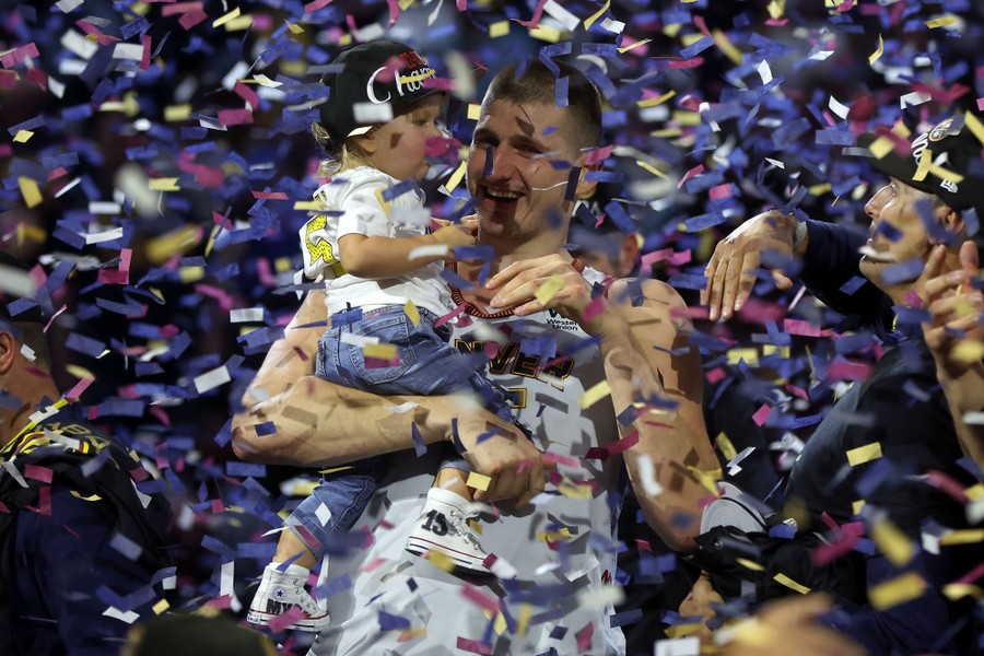 A basketball player holds his young daughter in a flurry of confetti.