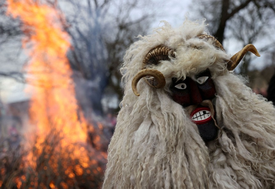 A person wearing a wooly costume and mask stands near a bonfire.
