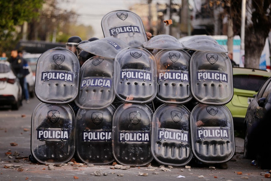 About a dozen riot police officers hold up plastic shields in a tight formation in a street.