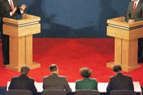 Two people debating at lecterns, with a panel of four people between them.