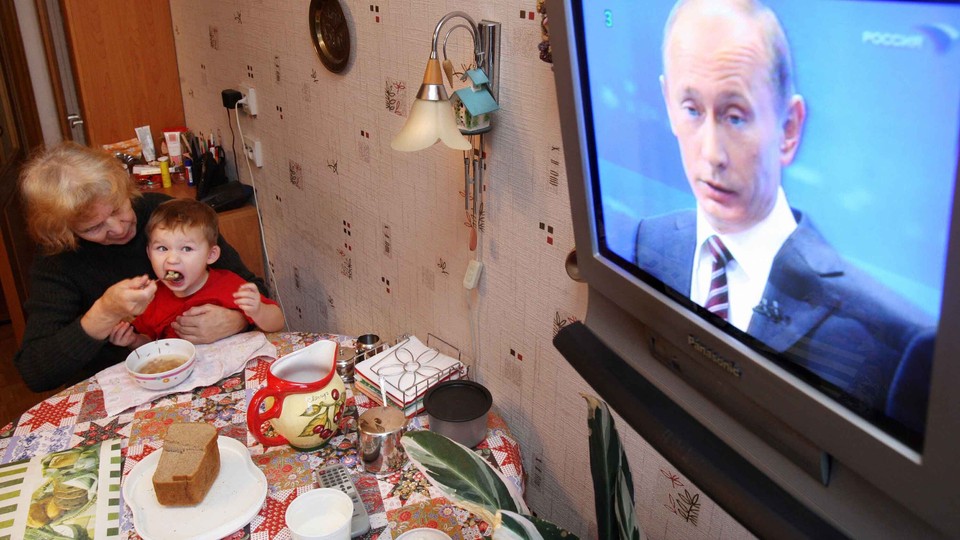 Photo of an elderly woman feeding a baby with Vladimir Putin on T.V.