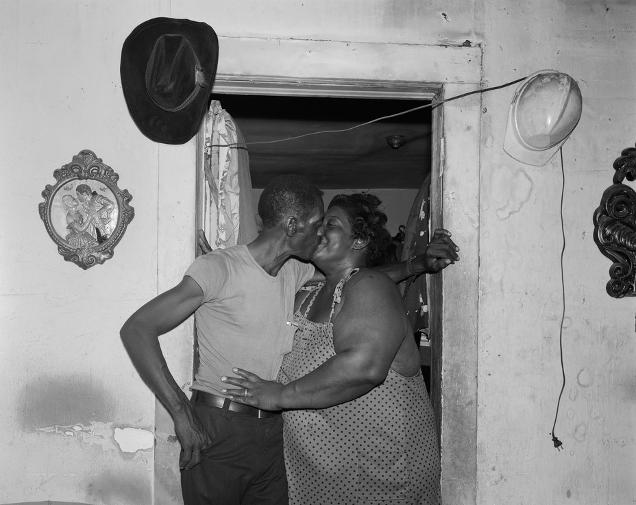 a couple kissing in a door frame with a cowboy hat and hard hat hanging on the wall