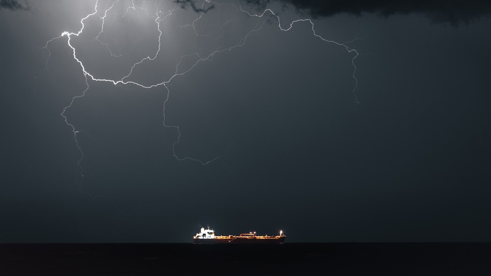 Color photograph of a huge lightning formation lighting up the night sky above an oil tanker
