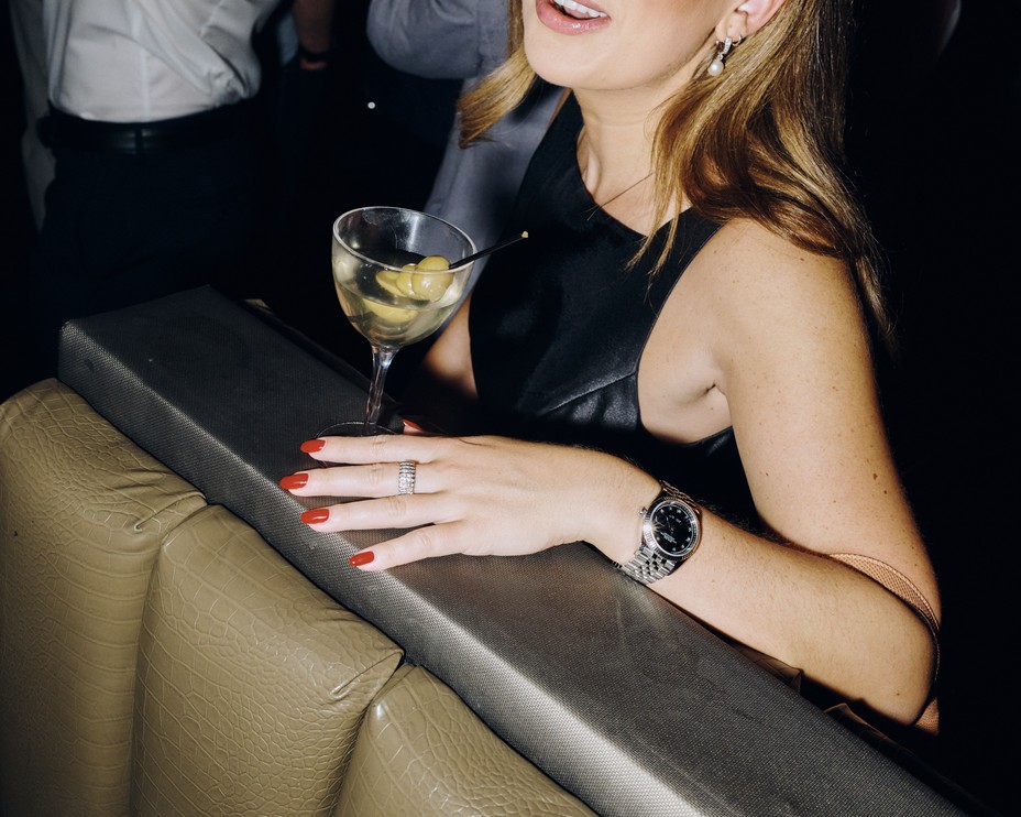 A color photograph of a woman in a black dress with red nails holding a martini