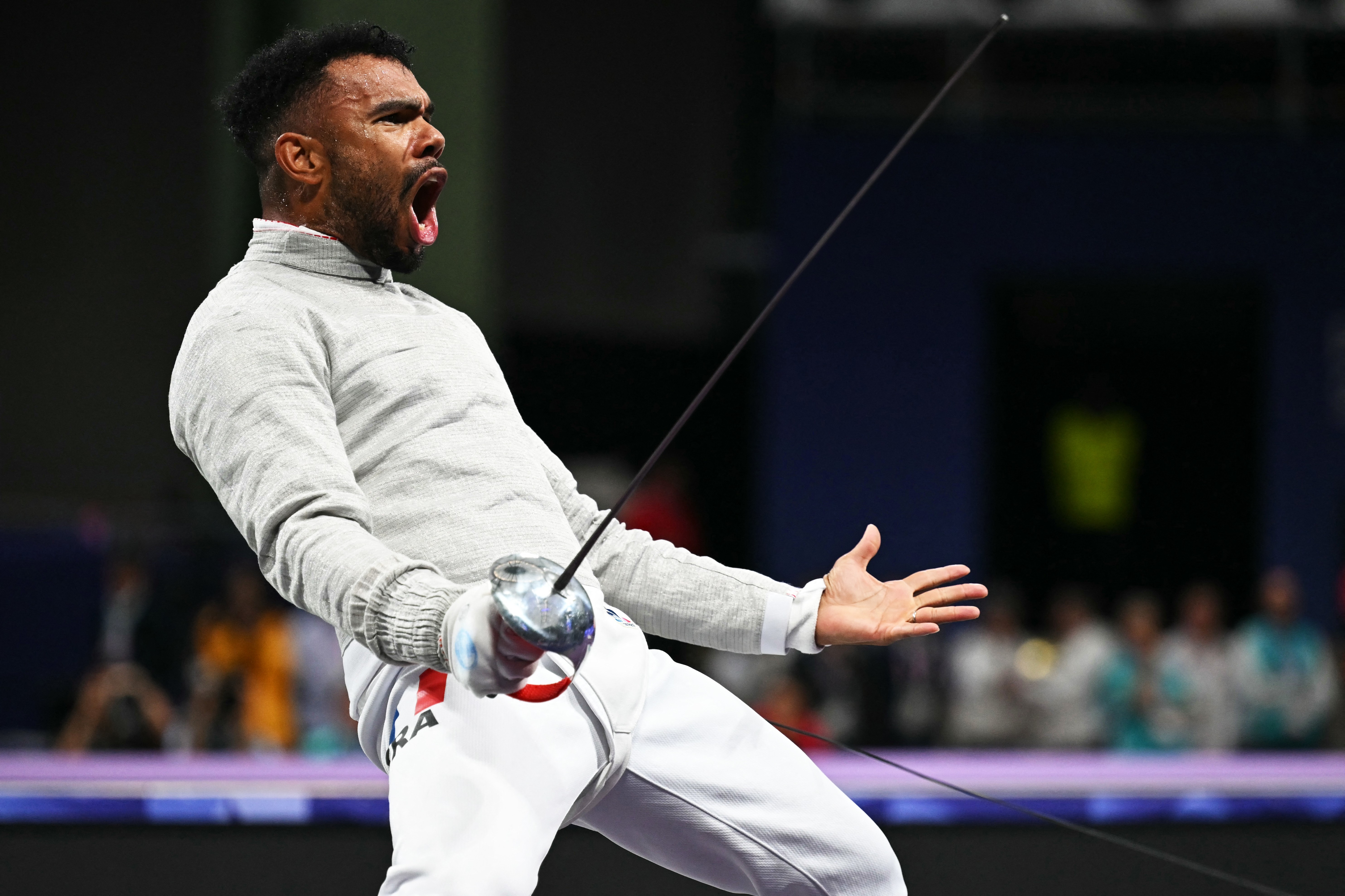 A fencer reacts after a match, arms outstretched, and mouth open.