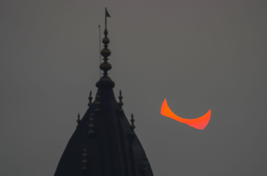 A partly eclipsed sun, seen behind a temple at sunset, appearing somewhat like a pair of red horns on the horizon
