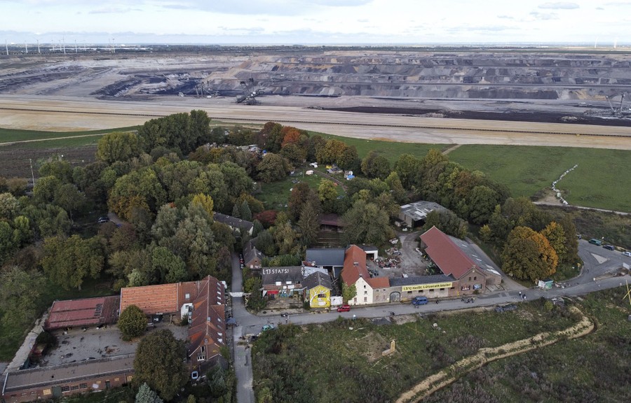 An aerial view of a small farm village beside a vast open coal-mine pit.