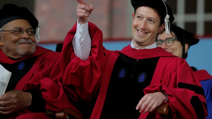 The Facebook founder Mark Zuckerberg points and smiles while wearing a cap at gown at Harvard's commencement