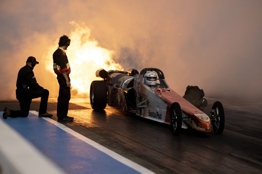 A drag-racing car powered by a huge jet engine blasts fire while sitting at a starting line.