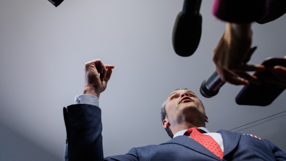 A photo shows Pete Hegseth surrounded by microphones