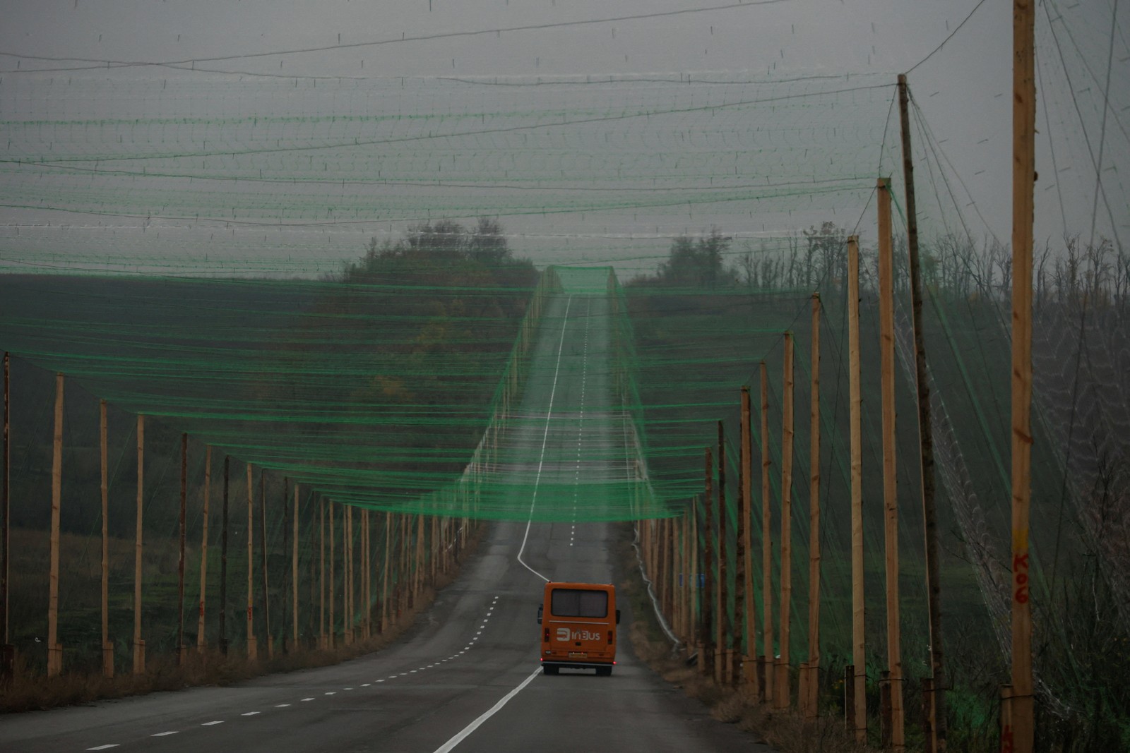 A car drives along a road covered with anti-drone netting, supported by tall poles on either side of the road.