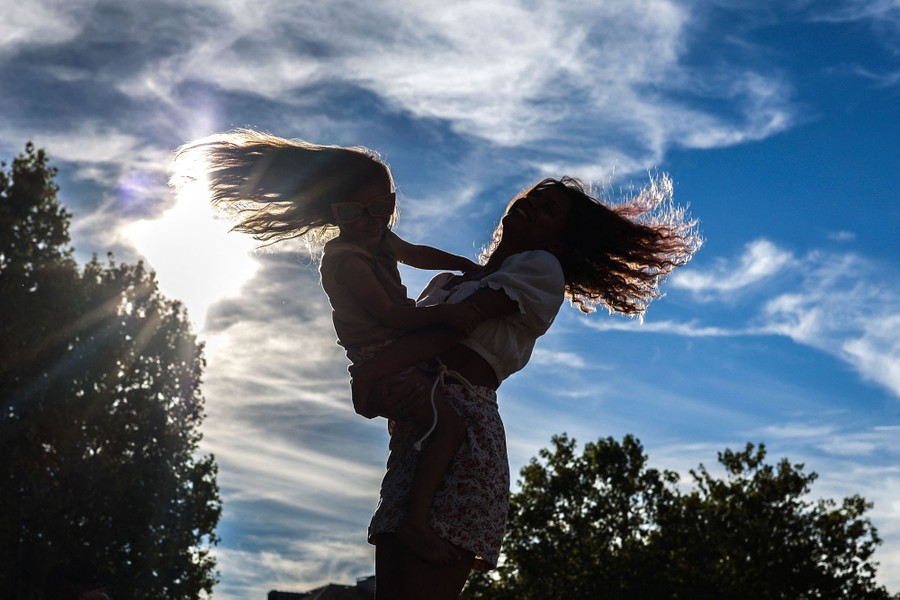 A woman dances with a child, spinning under a partly cloudy sky..