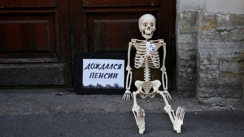 During Russian protests against the raised retirement age, a fake skeleton is seated next to a sign that says, "Waited for the pension."