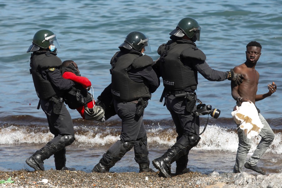 Soldiers carry and escort people along a beach.