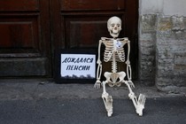 During Russian protests against the raised retirement age, a fake skeleton is seated next to a sign that says, "Waited for the pension."