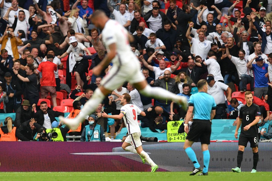 Fans cheer as England players celebrate on the field after scoring.