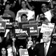 A black-and-white image of Donald Trump at a rally with supporters in the background.