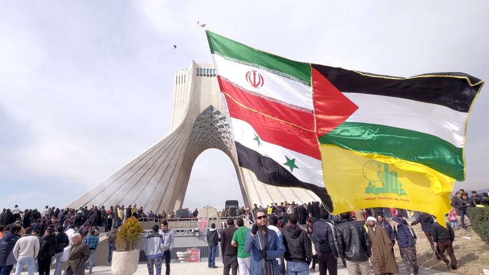 A man carries a giant flag made of flags of Iran, Palestine, Syria and Hezbollah in Tehran.