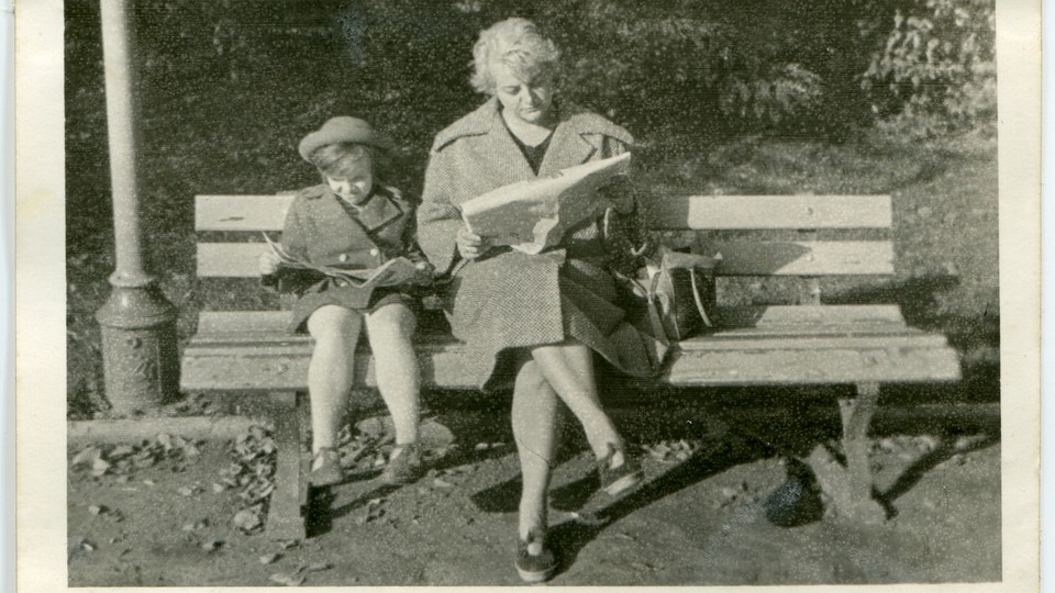 A vintage photo of a woman and a child reading books on a bench
