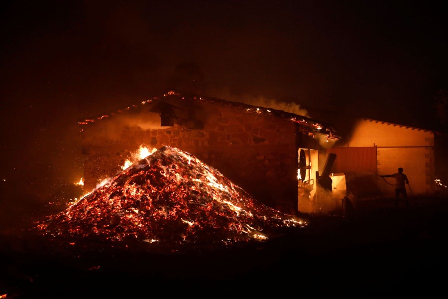 A building and nearby debris outside burns at night.