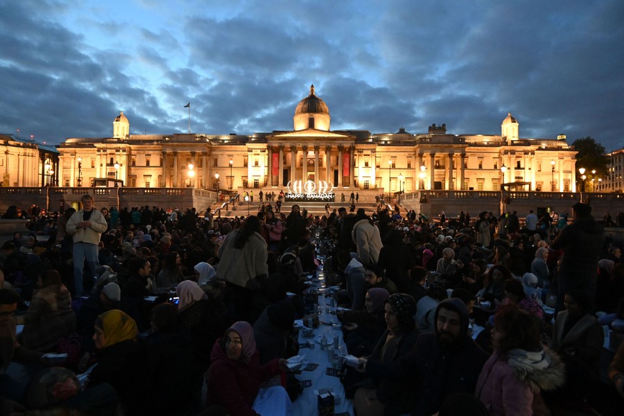 A large crowd of people is gathered at long tables in London's Trafalgar Square.