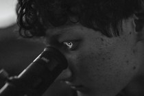 black-and-white photo of person looking into lens of telescope with reflected image lighting up the iris of their eye