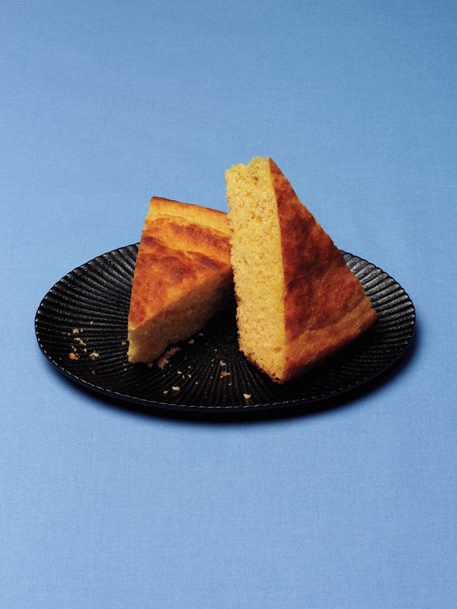 photo of 2 wedges of cornbread on black plate with blue background