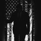 A black-and-white image of Donald Trump silhouetted in front of a draped American flag