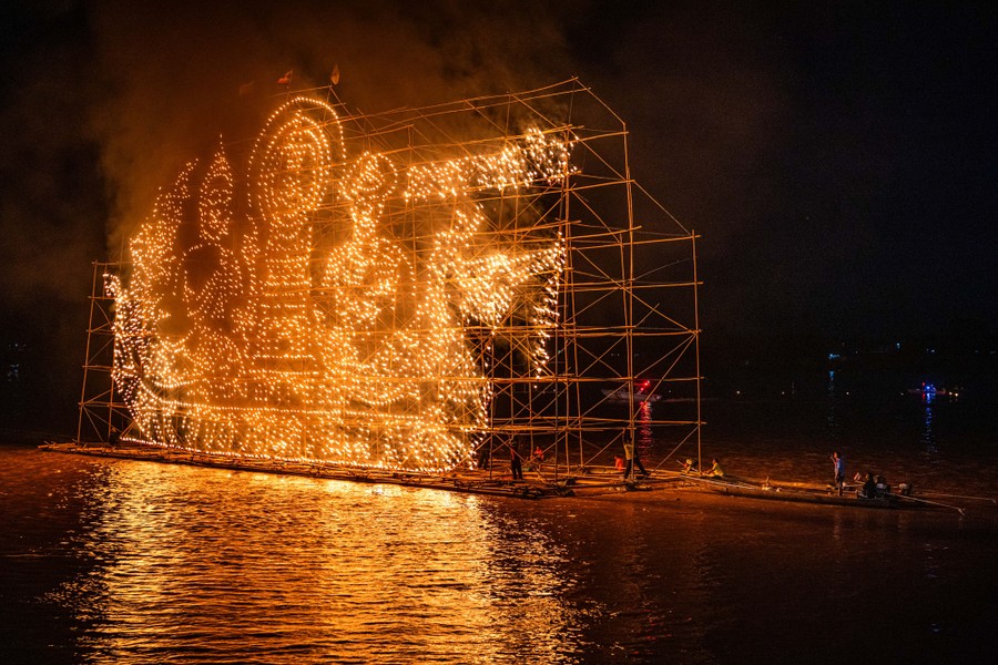 A floating platform supports tall scaffolding that has been decorated with oil candles that form an image of people in a boat.