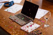 Confetti is strewn across a laptop, notebook, and wine glass