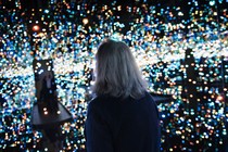 A woman alone in an art installation with hundreds of tiny lights and mirrored walls.