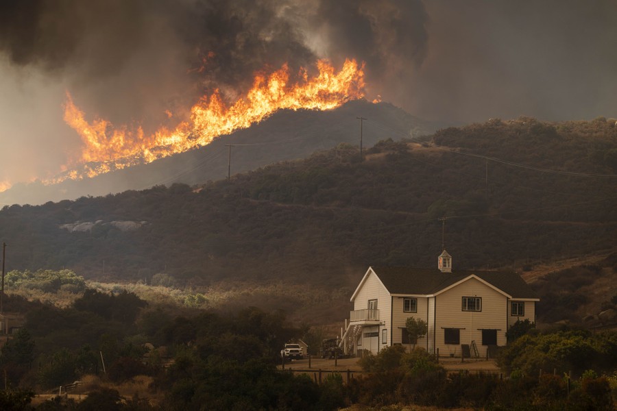 A view of a house on a hillside, with a large wildfire burning above it