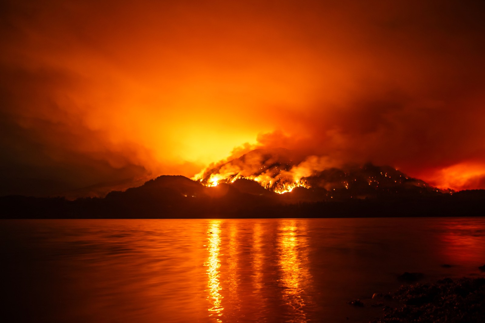A nighttime view of a wildfire burning on a mountain across a body of water.
