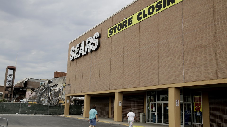 Two people walking into a Sears store that is slated to close