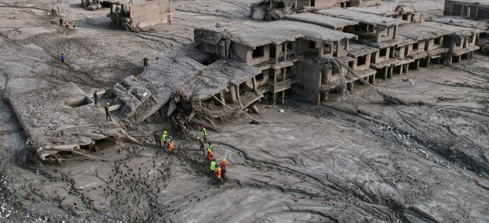 A drone view of rescue workers inspecting damaged and mud-covered structures