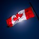 A Canadian flag, slightly darkened by the light, waves in the air.
