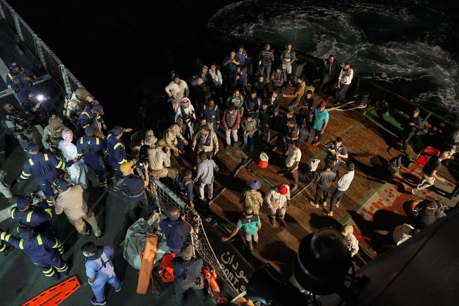 Navy sailors help civilians transfer from the deck of one ship to another.