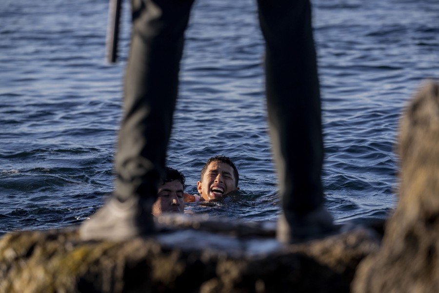 Migrants swim toward a soldier who waits on shore.