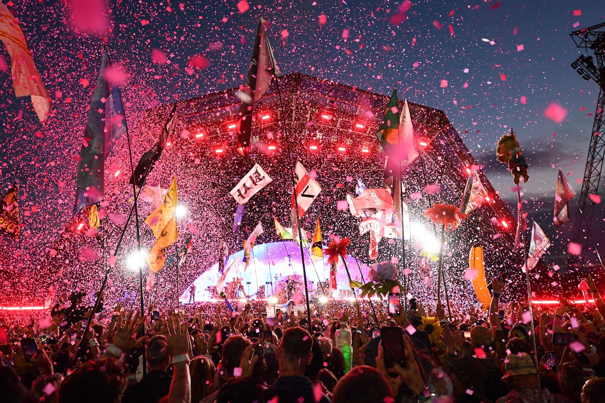Confetti flies above a crowd listening to Coldplay perform at an outdoor stage.