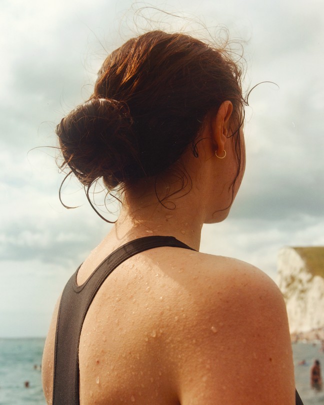 Image of the back of a girl's head as she looks towards the coast