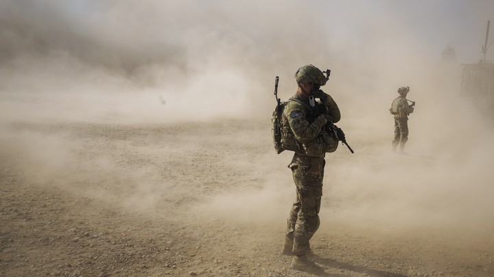 U.S. soldiers cover their faces from the dust blown around by the rotors of a helicopter.