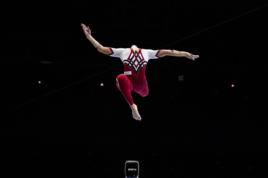 A gymnast in midair as they jump, their arms outstretched and their head tipped back