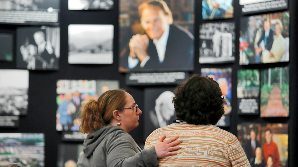 A mourner is comforted near a display of pictures of Billy Graham in Asheville, North Carolina, in 2018. 