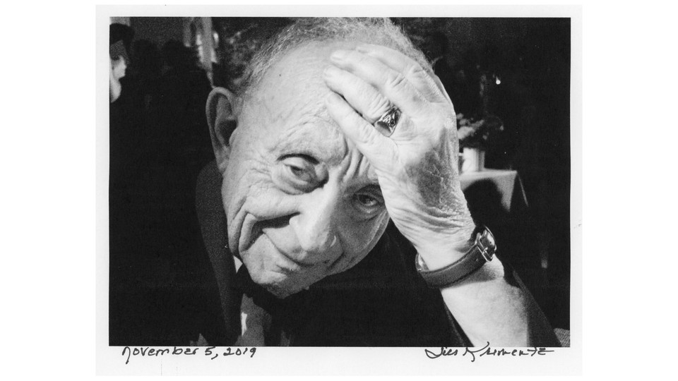 In a black and white photo a man holds his head in his hands and smiles