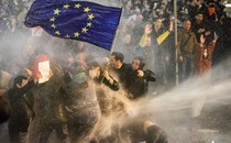 Protesters holding a European Union flag brace as they are sprayed by a water cannon.